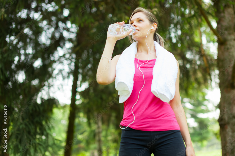 Woman drinking water while running in a park Woman drinking water while running in a park