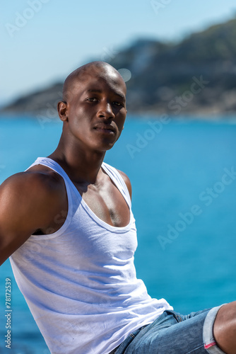 Sitting African black man by ocean on rock