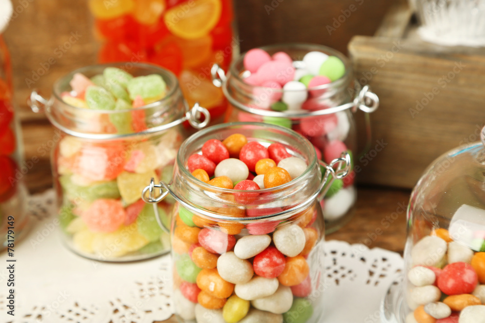 Multicolor candies in glass jars on wooden background Multicolor candies in glass jars on wooden background