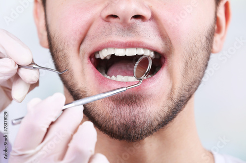 Examine of young man by dentist on white blurred background