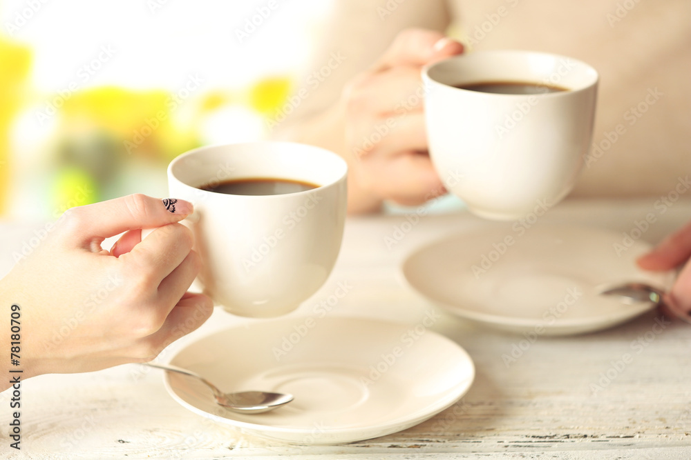 Two women with cups of coffee on bright background Two women with cups of coffee on bright background