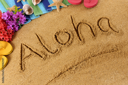 The word Aloha written in sand on a beach with towel flip flops seashells Hawaii summer vacation holiday photo
