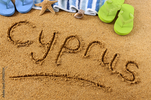 The word Cyprus written in sand on a beach with towel flip flops seashells summer vacation holiday photo