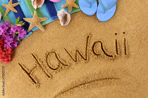 The word Hawaii written in sand on a beach with towel flip flops seashells Hawaiian summer vacation holiday photo