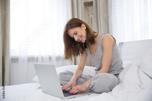 Happy smiling woman using laptop on the bed at home