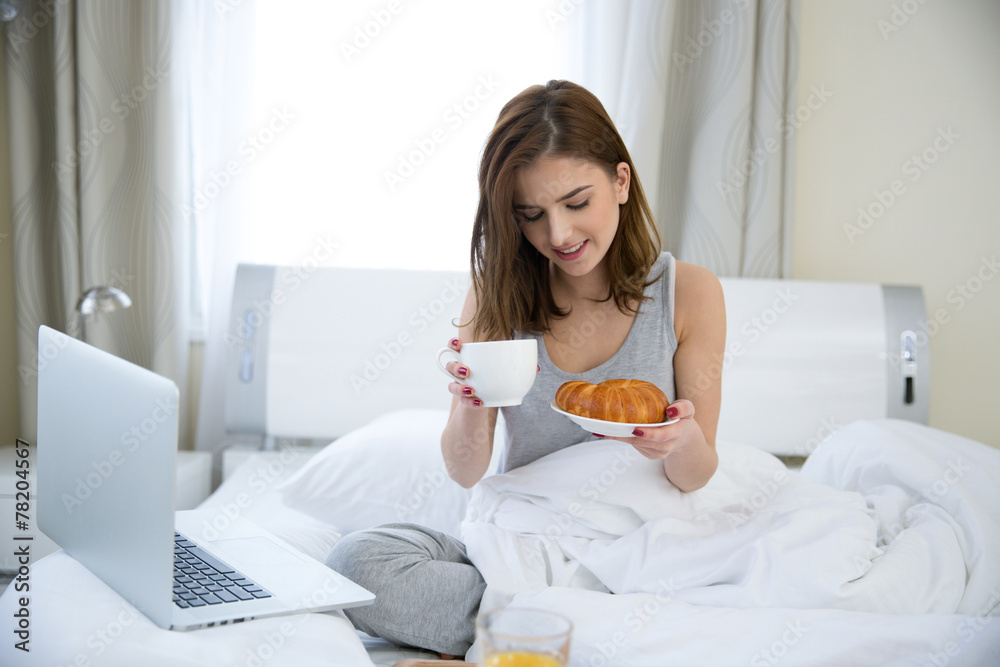 Smiling woman sitting on the bed with breakfast Smiling woman sitting on the bed with breakfast
