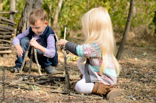 Little boy and girl playing in woods with sticks
