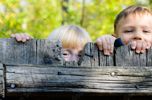 Two children peeking over a wooden fence