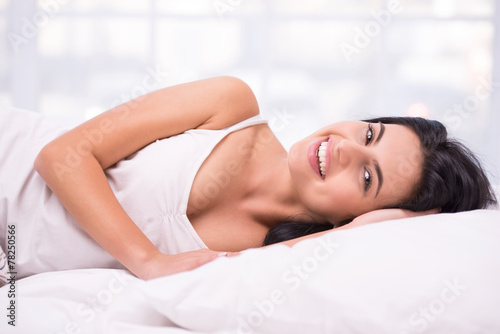 Young dark haired woman smiling in white bed