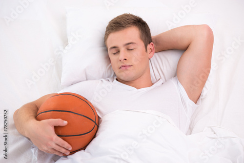 Young man sleeping in bed with basketball