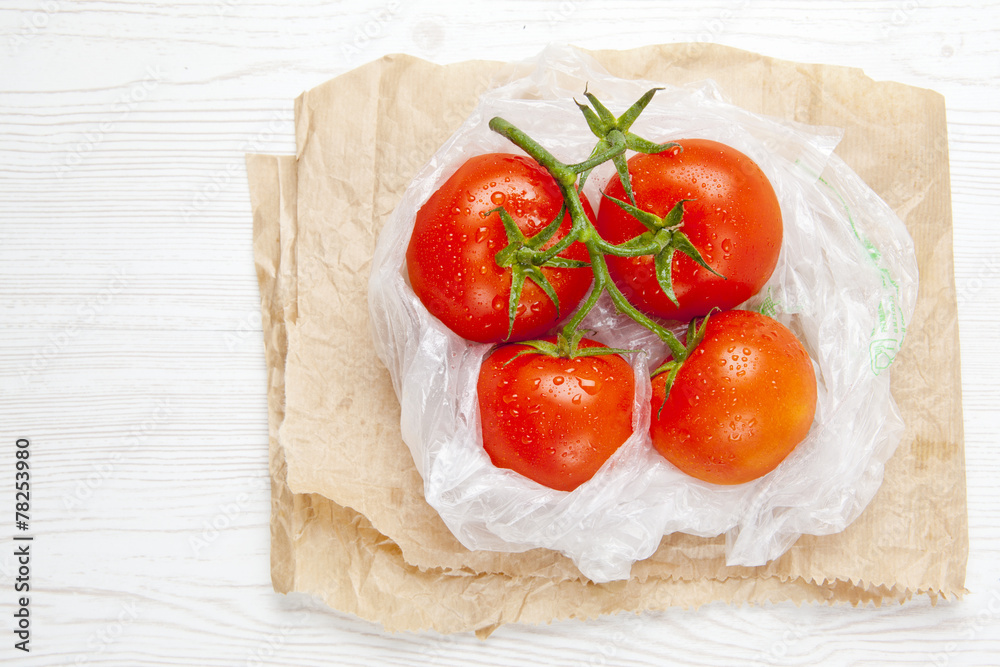 fresh ripe large wet tomatoes in plastic bag on a white wooden b