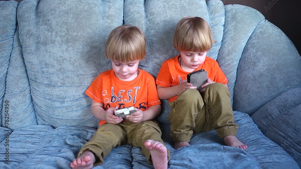 Kids twins having fun playing with mobile cell phones on a couch Kids twins having fun playing with mobile cell phones on a couch