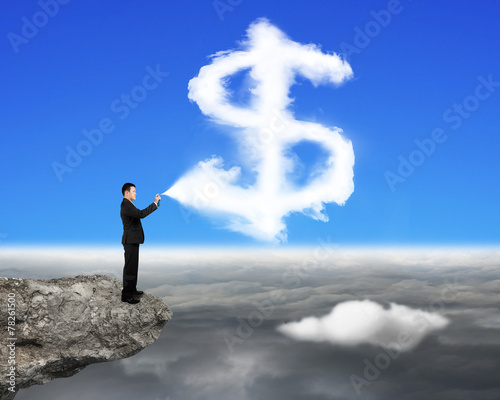 Businessman spraying dollar sign shape cloud paint on the cliff