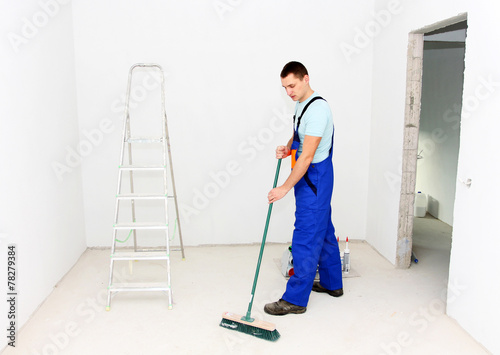 Young man cleaning floor with brush after repair