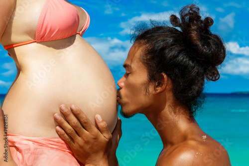 Happy and young pregnant couple having fun on a tropical beach.
