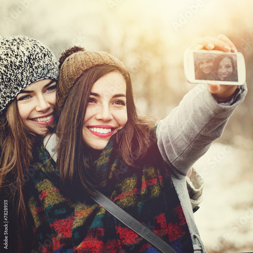 Two teenage girls taking a selfie outdoors in winter