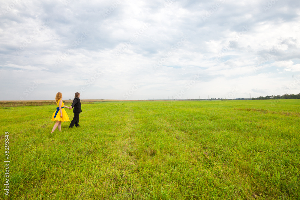 girl in yellow dress follows man in black suit on the field