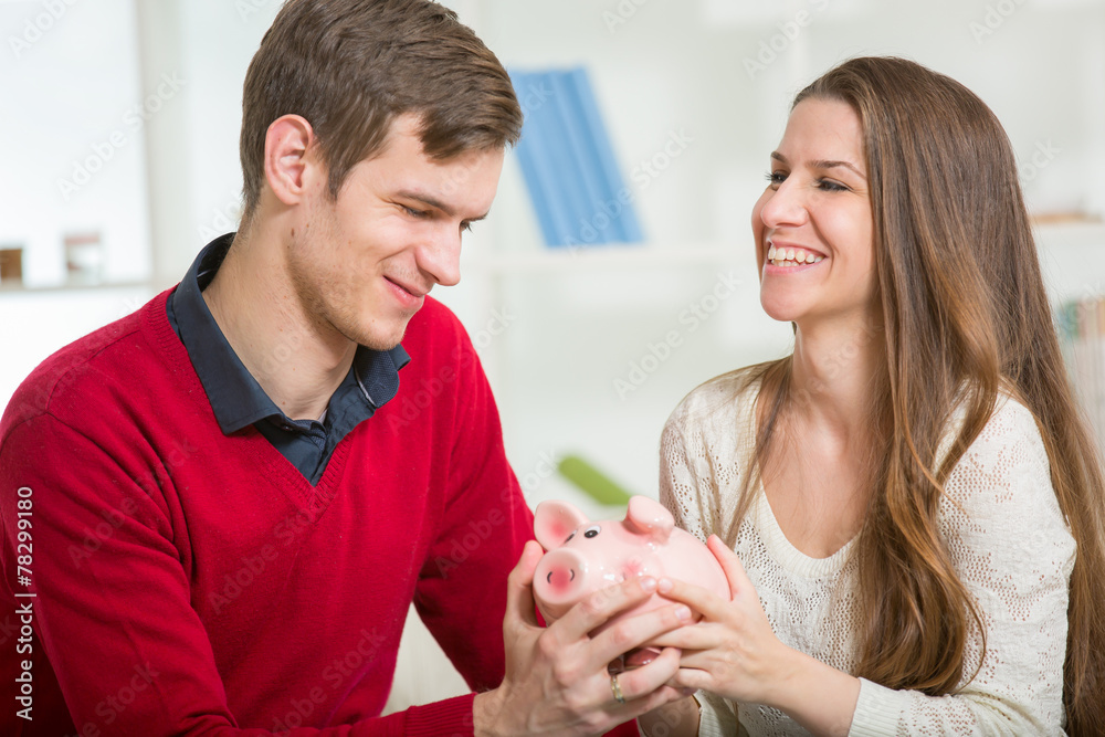 Young happy couple holding a piggy bank in the living room Young happy couple holding a piggy bank in the living room