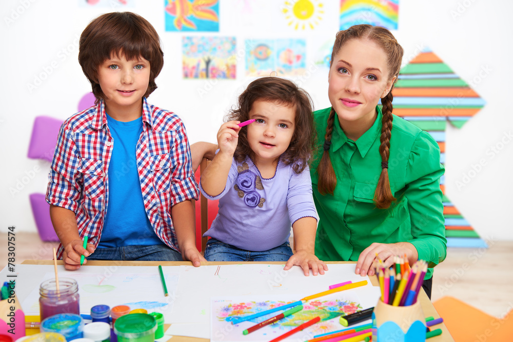 Fototapeta premium Teacher with children drawing and looking at camera