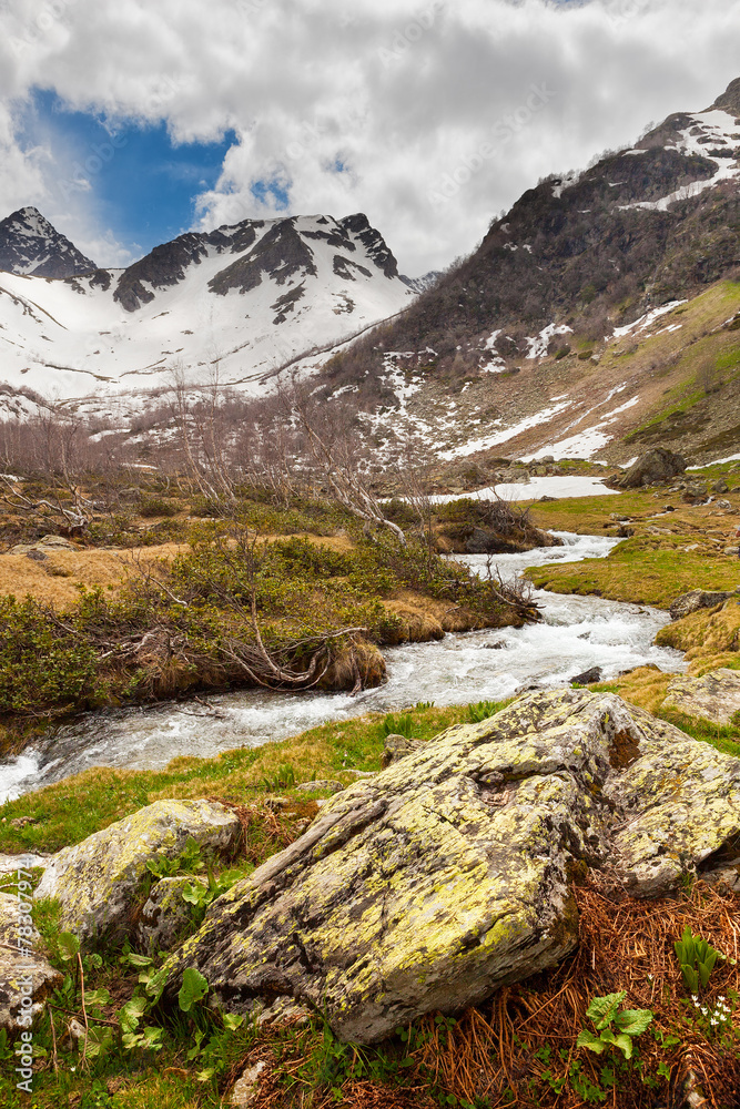 View to snow on Caucasus mountains over clear water stream near