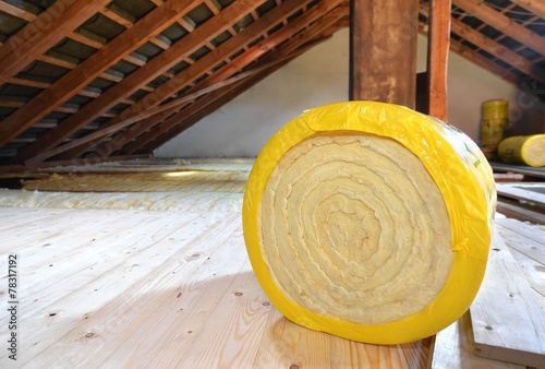 A roll of insulating glass wool on an attic floor photo