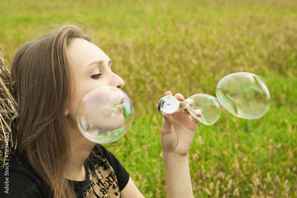 young girl sitting on the grass and blowing soap bubbles
