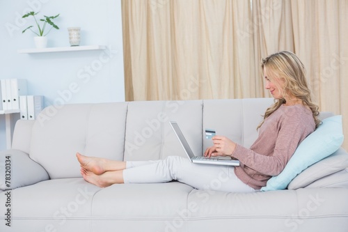 Smiling blonde shopping online with laptop