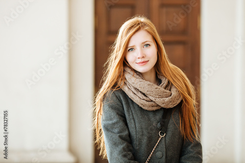 Young redhead woman wearing coat and scarf posing outdoors
