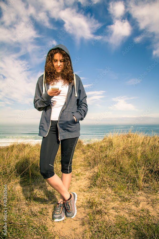 Young woman with hoodie and sportswear looking smartphone Young woman with hoodie and sportswear looking smartphone