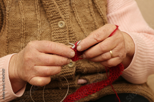 Elderly woman knitting with red wool.
