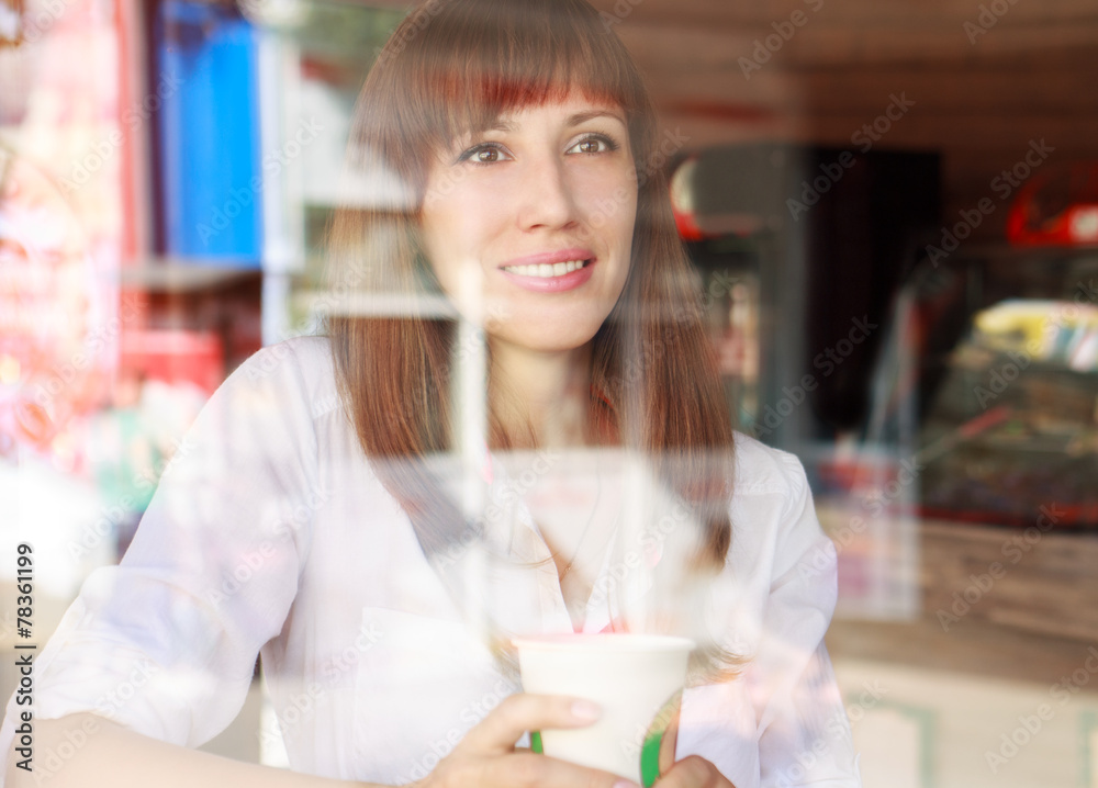Young smiling woman behind glass of cafe