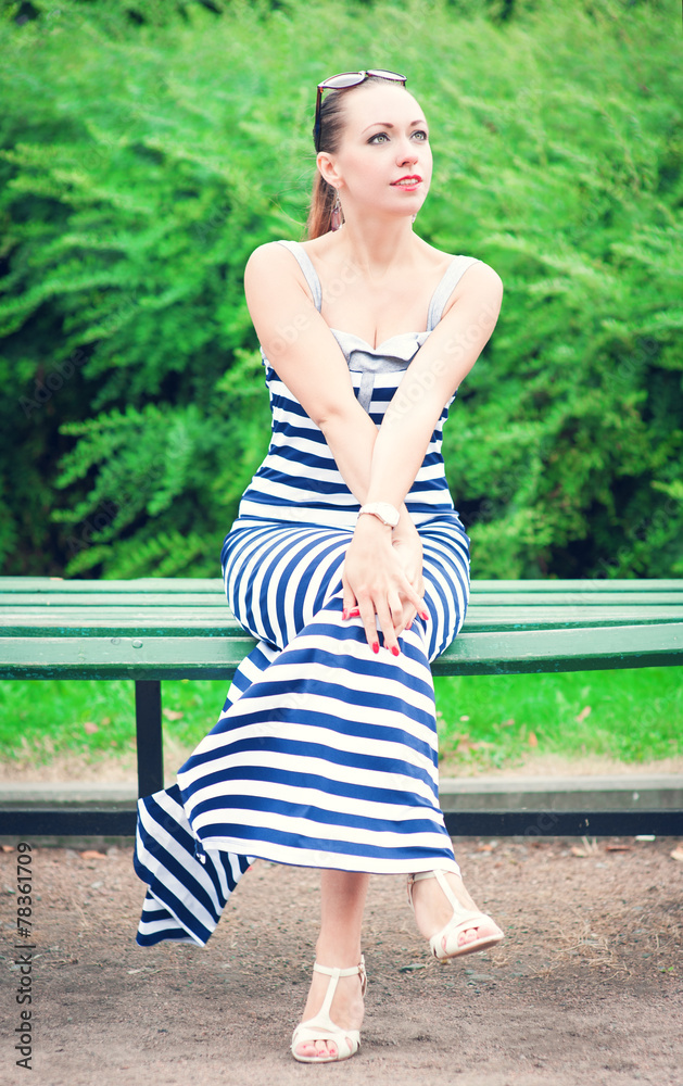 Naklejka premium Young beautiful fashionable woman wearing striped dress sitting