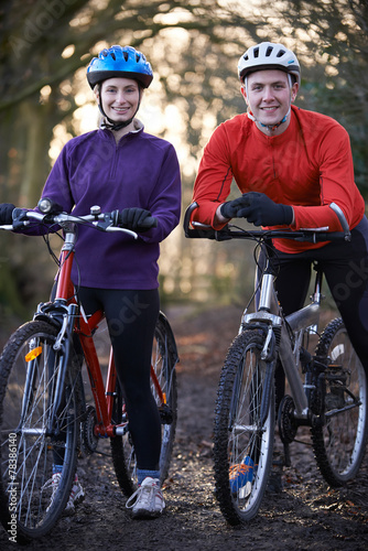 Couple Riding Mountain Bikes Through Woodlands