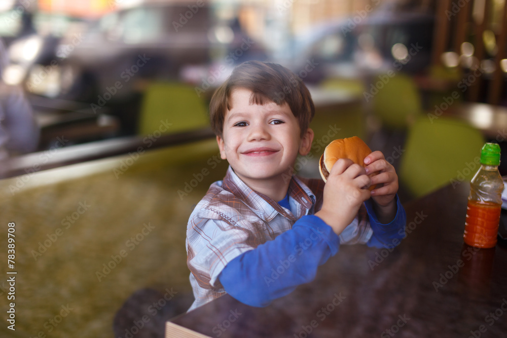Fototapeta premium Little boy smile with hamburger in fast food restaurant