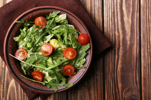 Salad with arugula and cherry tomatoes on wooden table
