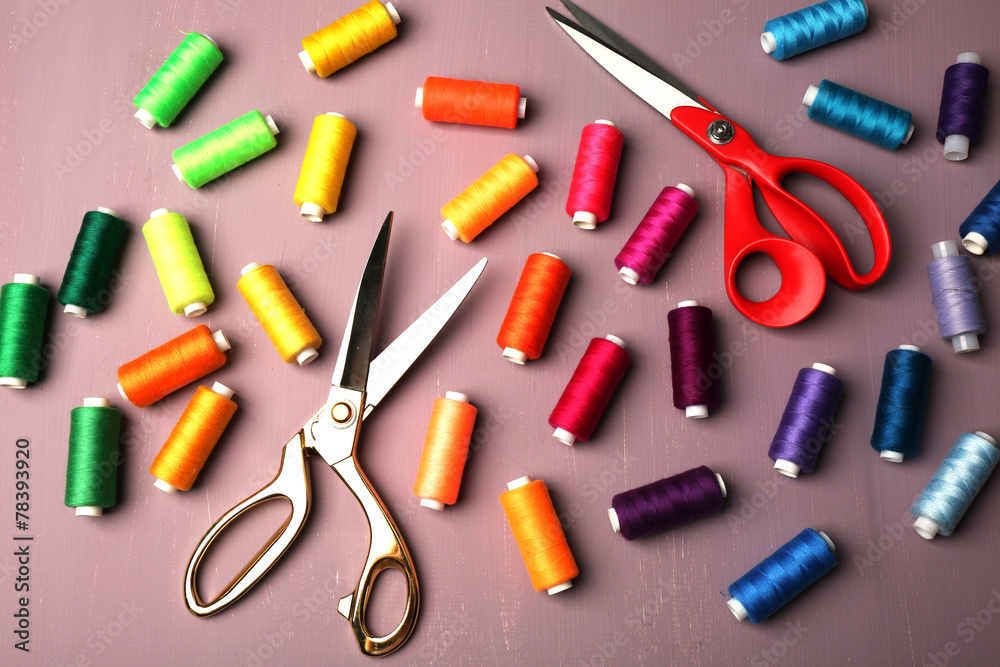 Multicolor sewing threads with scissors on wooden background