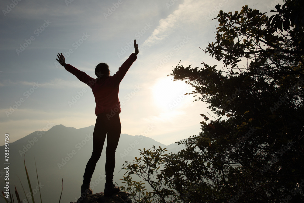 cheering woman open arms at sunrise mountain peak