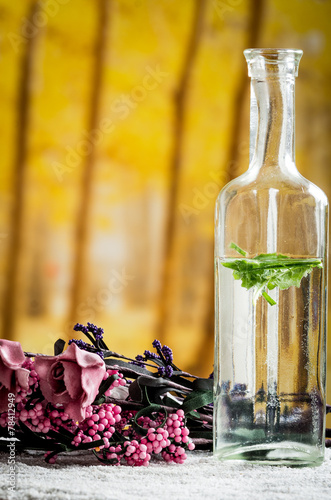 glass bottle with leaves inside and flowers in the background