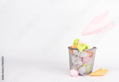 isolated wastebasket full of waste paper and paper airplane
