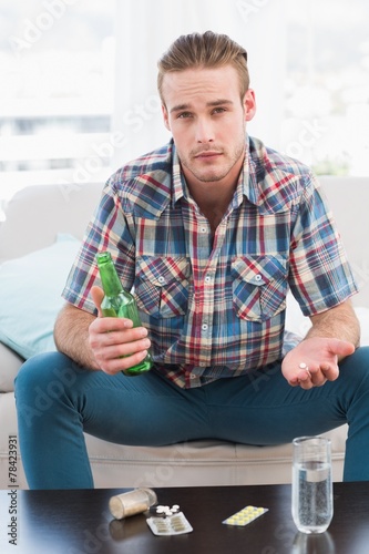Unsmiling man with a beer and his pills