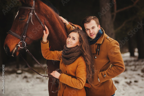 stylish couple in bright coat with a horse