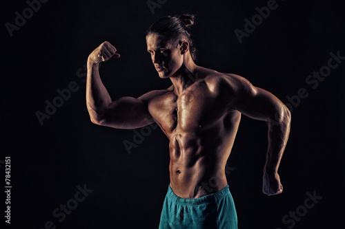 Handsome muscular bodybuilder posing over black background. © romanolebedev