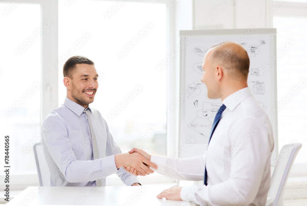 two smiling businessmen shaking hands in office two smiling businessmen shaking hands in office