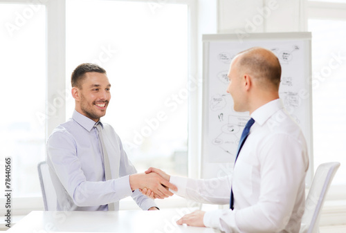 two smiling businessmen shaking hands in office