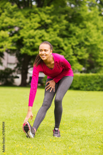 smiling black woman stretching leg outdoors