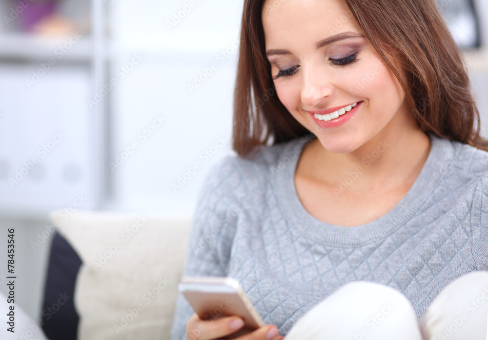Pretty girl using her smartphone on couch at home in the living Pretty girl using her smartphone on couch at home in the living