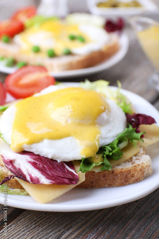 Toast with egg Benedict and tomato on plate on wooden table Toast with egg Benedict and tomato on plate on wooden table