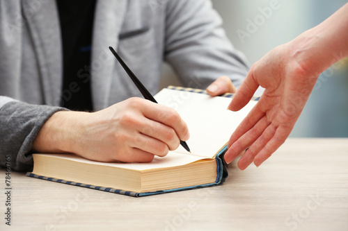 Author signing autograph in own book at wooden table photo