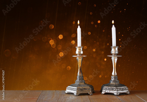 two candlesticks with burning candles over wooden table and vint
