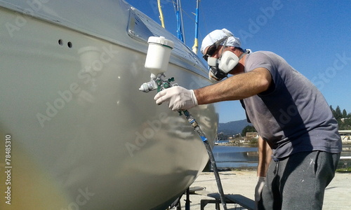 man with face mask spray painting sail boat yacht with air gun	